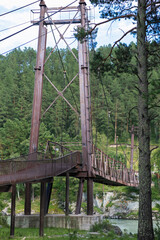 A wooden bridge with metal supports across a raging river in the Altai Mountains. Old broken bridge
