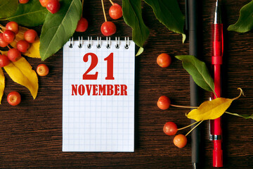 calendar date on wooden dark desktop background with autumn leaves and small apples. November 21 is...