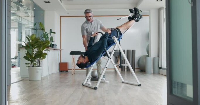 Inversion, table and man in therapy for back pain, healing and chiropractor helping and stretching spinal muscle in clinic. Physiotherapy, doctor and patient in rehabilitation for spine with gravity
