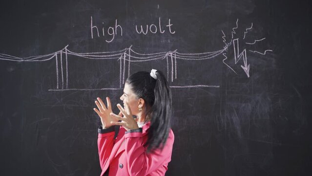 The woman who writes High Volt on the blackboard looks nervously at the camera.
