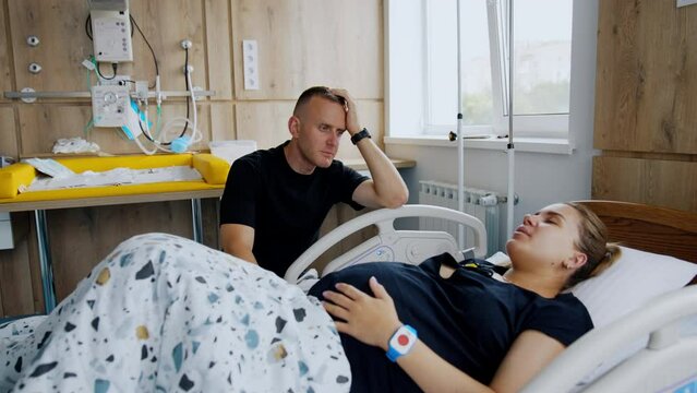 Man supporting his wife at the beginning of labor. Man sits at woman's bed at hospital talking to her.