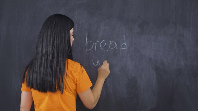 Woman writing waste of bread on blackboard looks at camera with frustration.