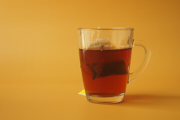 Cup of tea with tea bag on orange color background 