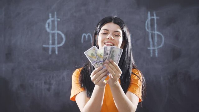 Woman writing Money on blackboard looks at camera with happiness.