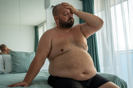 Depressed obese man feels overworked body due to metabolic disorder. Tired fat male puts hand on head suffers chronic fatigue, headaches, dyspnea, increased blood pressure. Eating disorder problem.
