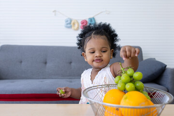 A curly-haired African toddler learns to pick fruit and eat it herself.