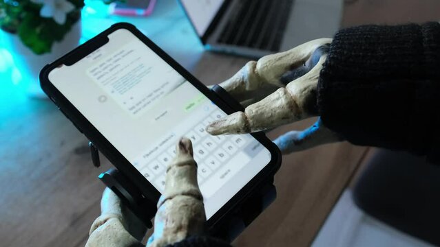 Hands in skeleton costume holding for smartphone fast typing and send message in chat, social networks. Halloween party, technology and social media.