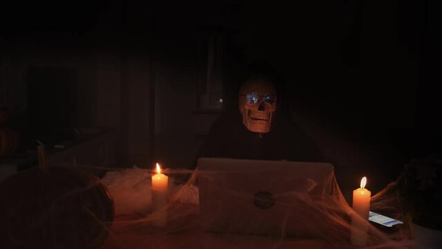 Celebrating holiday, terribly spooky Halloween background, death in fog show rock sign, laptop and candles in cobwebs. Copyspace, vignette. Halloween invitation truly frightening and unforgettable.