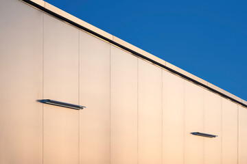 Fluorescent light tubes on aluminum composite wall outside of modern office building against blue sky background