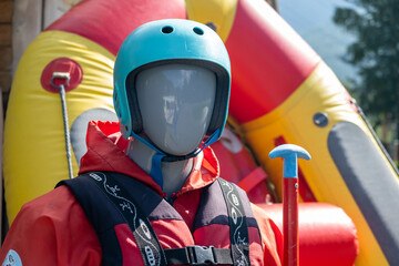 A mannequin in a red life jacket next to an inflatable boat as an advertisement for rafting or...