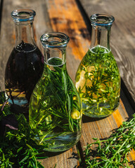 A composition of bottles with rosemary, thyme, basil oil on a blurry background. Rosemary, basil, thyme oil fry in olive oil. Bottles of oil on a wooden table. Selective focus.