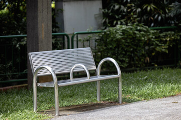 A metal bench stands in the park on the street, there are no people around, behind the bench you...