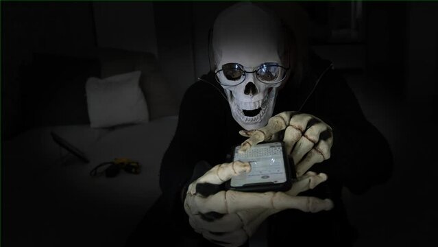 Scary skeleton with bone fingers typing messages on screen of smartphone, close up. Dark background. Happy Halloween, technology and social media integral parts of modern-day celebrations.