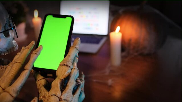 Close up, hands in bone costume using smartphone and social networks in blurred background. Celebrating holiday Halloween. Horror-loving friends to scariest Halloween party.