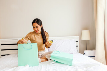 Happy lifestyle beautiful Asian woman sitting looking at her beautiful expensive French perfume bottle design from luxury shopping paper bag french perfume cosmetics at home.