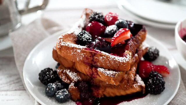Garnishing stack of freshly made french toast garnished with mix berry compote and powder sugar.