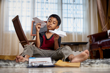 Boy playing handmade paper airplane at home