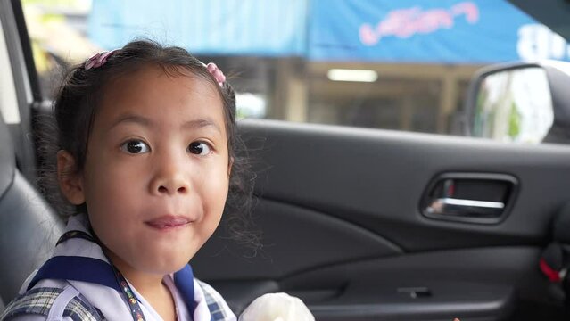 Small girl in school uniform sitting in car eating sticky rice with grilled pork satay.