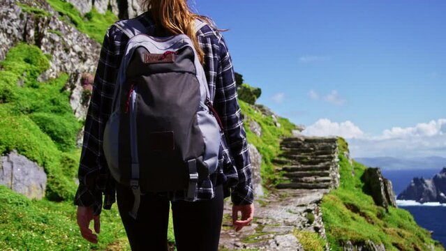 Woman with backpack hiking cliff face in Ireland