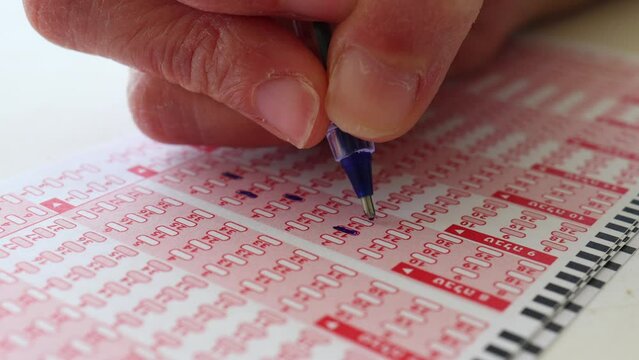 Woman hand marking numbers on Lottery Ticket with Pencil.