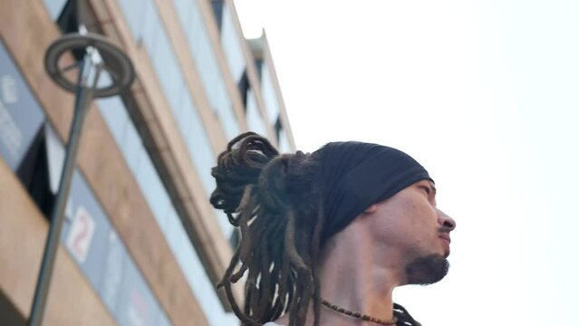 Looking up young cute stylish guy with dreadlocks, earrings in his ears and beads getting lost in the city is at a loss and looking for the right address turning his head with sharp movements