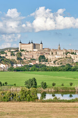 Fototapeta na wymiar Image of the old town of Toledo with detail of the eastern area with the fortress dominating the urban landscape with green fields and the Tagus River in the foreground