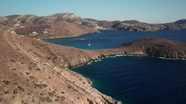 Drone trucking pan of syros greece coastline, deep blue water contrasting tan dry mountainous landscape