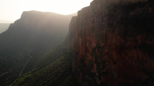 Aerial push in as light streams above mountain casting glowing rays to leonidio greece rocky cliffs