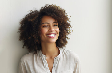 A young biracial of African-European woman in cotton fiber shirt smiling against a white wall, concept of 
aesthetic beauty 