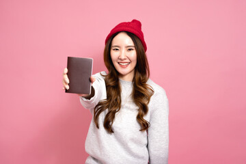 Beautiful asian female passenger in sweater, jeans, and beanie hat. Portrait of a smiling girl showing passport in half length size. Winter lifestyle and travel concept - 644343952