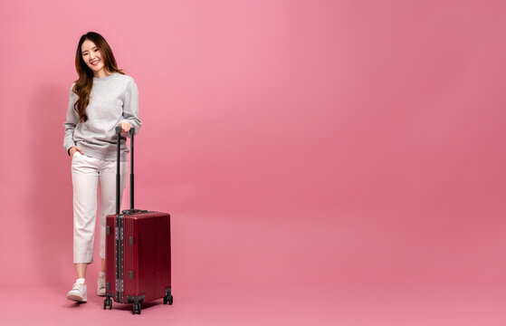 Beautiful asian female passenger in sweater, jeans, and luggage. Portrait of a smiling girl with luggage in full length size. Winter lifestyle and travel concept