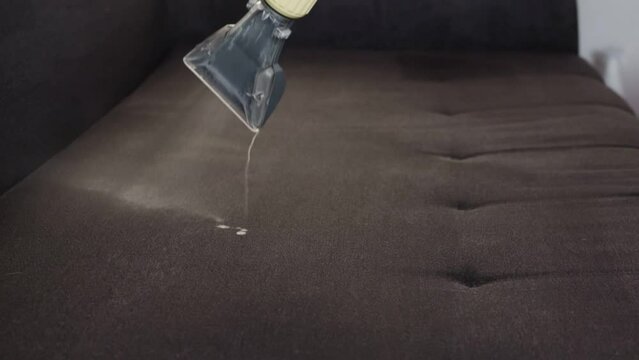 Applying a special cleaning solution to clean stains and dirt on upholstery of upholstered furniture. The first stage of dry cleaning. Slow motion. Copy space for text