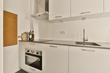 a kitchen with white cupboards and black counter tops on the wall behind it is a cork notice board attached to the door