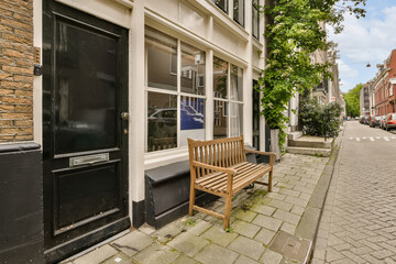 a wooden bench in front of a building on the side of a street with bricked buildings and green trees