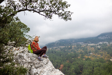 traveler girl sits on the edge of a cliff with an autumn forest and enjoys a beautiful view of the valley.