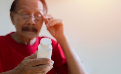 Closeup of Asian elderly male with presbyopia holding and looking at a pill container with confusion.