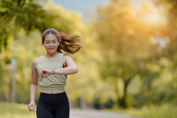 Beautiful Asian female jogger running in the park and looking at her watch to see her running timing in the park background.
