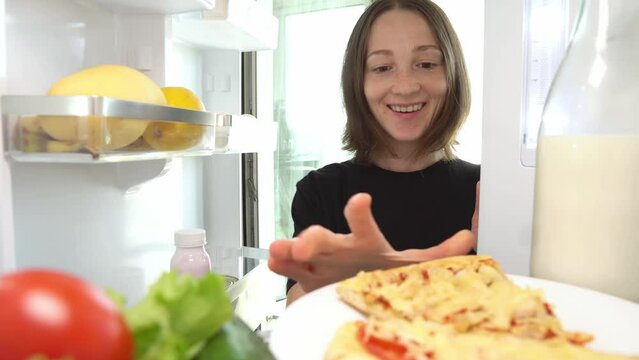 A woman opens a refrigerator with food to eat pizza instead of healthy vegetables. View from inside. The concept of eating junk food