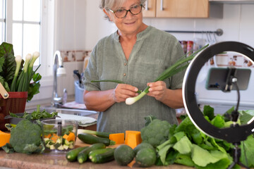Senior attractive woman streaming online by smartphone follows a vegetarian cooking class. Home...