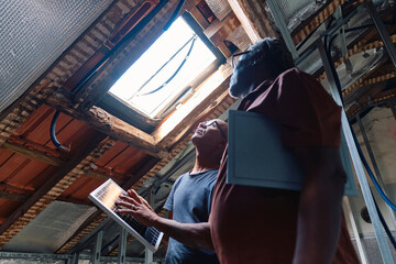 Architect and builder holding solar panel and looking through ceiling window in attic