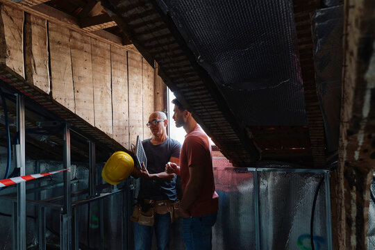 Construction worker holding solar panel and discussing with man in attic
