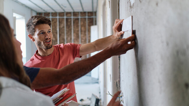 Man and woman discussing over sample tiles with construction worker on wall