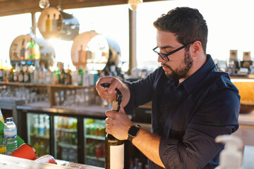 Young bartender opening bottle of wine at cafe