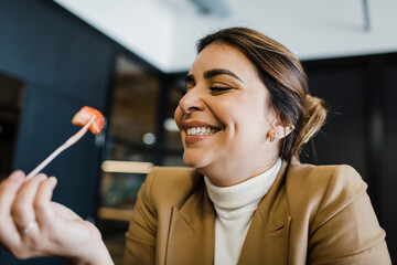 Happy businesswoman eating strawberry with fork at office