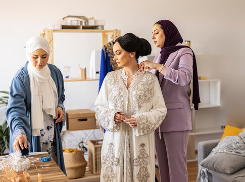 Fashion designer with colleague adjusting wedding dress on bride