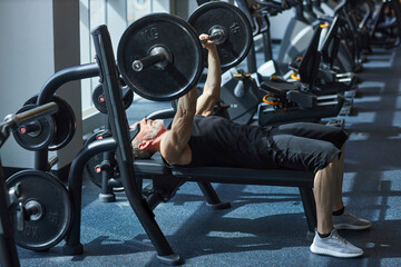 Mature man doing bench press exercise in gym