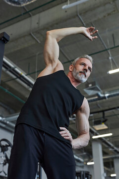 Dedicated mature man stretching hands in gym