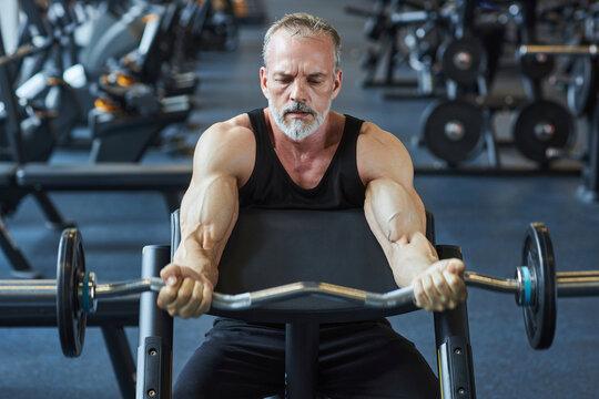 Mature man strengthening arms with barbell in gym