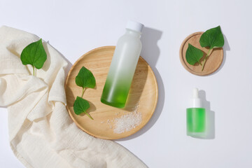 A glass bottle unlabeled on wooden plate decorated with fish mint leaves and cotton towel on a white background. Space for design, advertising and branding cosmetic product