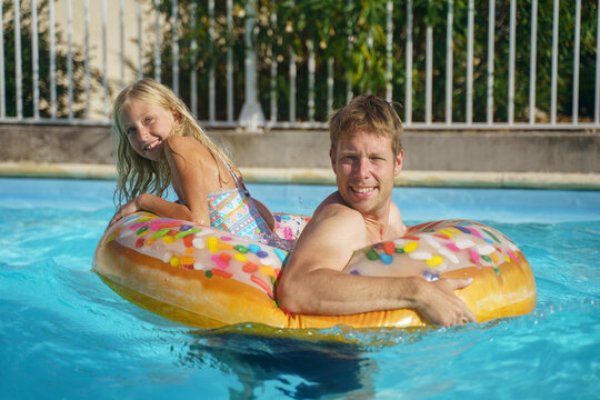 Smiling and daughter playing with inflatable ring in swimming pool